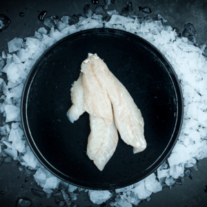 Fresh white fish fillets on a black plate surrounded by crushed ice, showcasing premium South Island seafood ready for cooking.