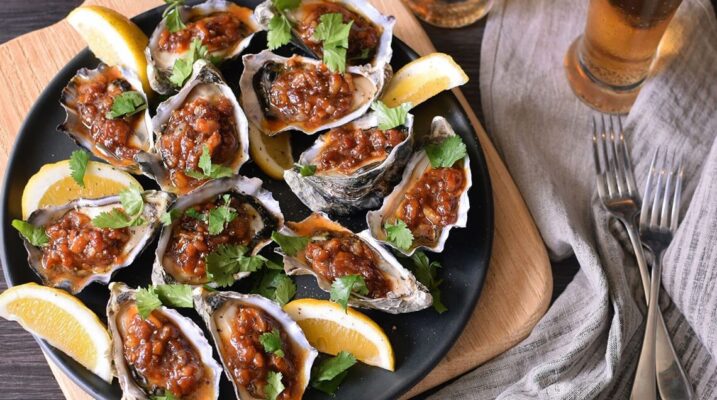 Oysters Kilpatrick topped with bacon, onion and tamarind chutney, served with lemon wedges and fresh coriander.