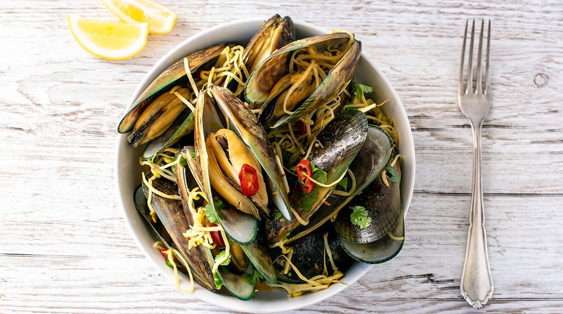 NZ Greenshell mussels in coconut tamarind sauce with bean sprouts, chilli and coriander, served in a bowl.
